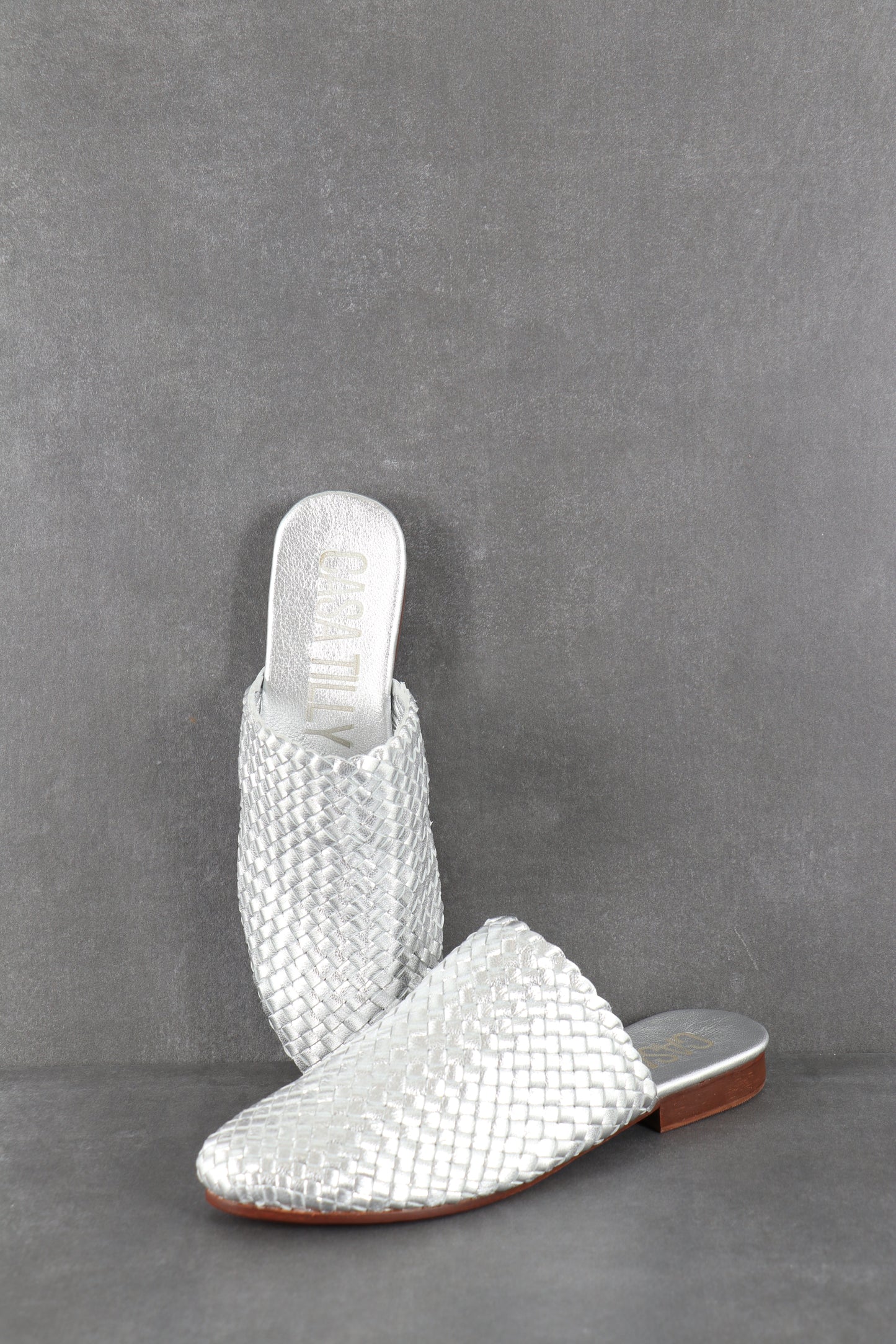 Mules plates tressées argent en cuir pour femmes.