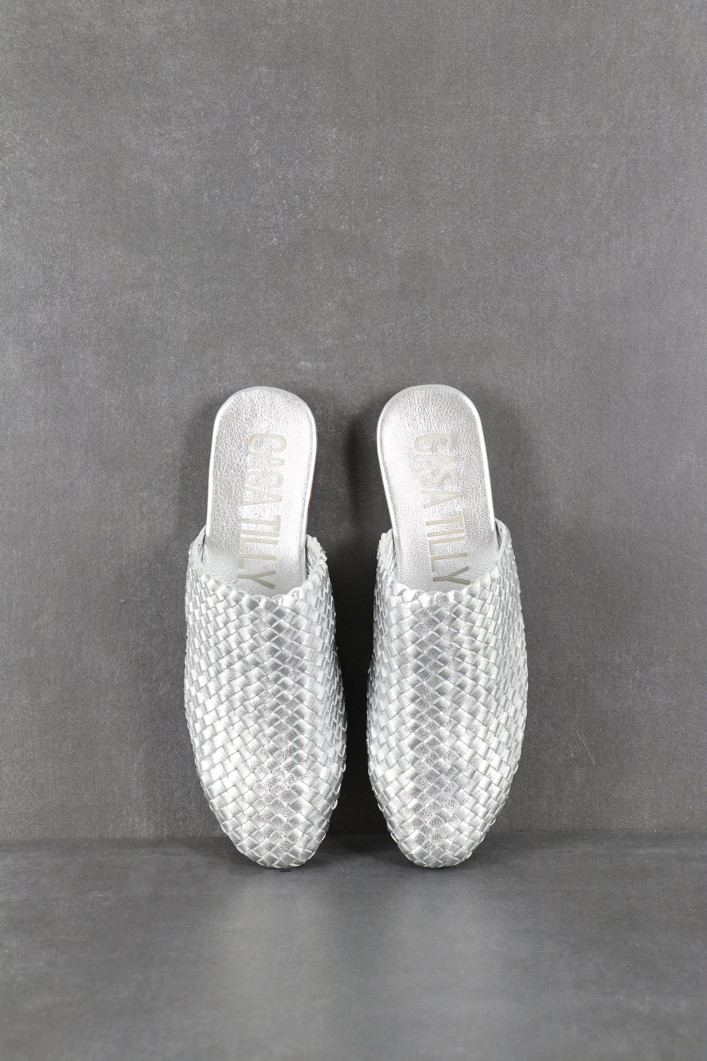 Mules plates tressées argent en cuir pour femmes.